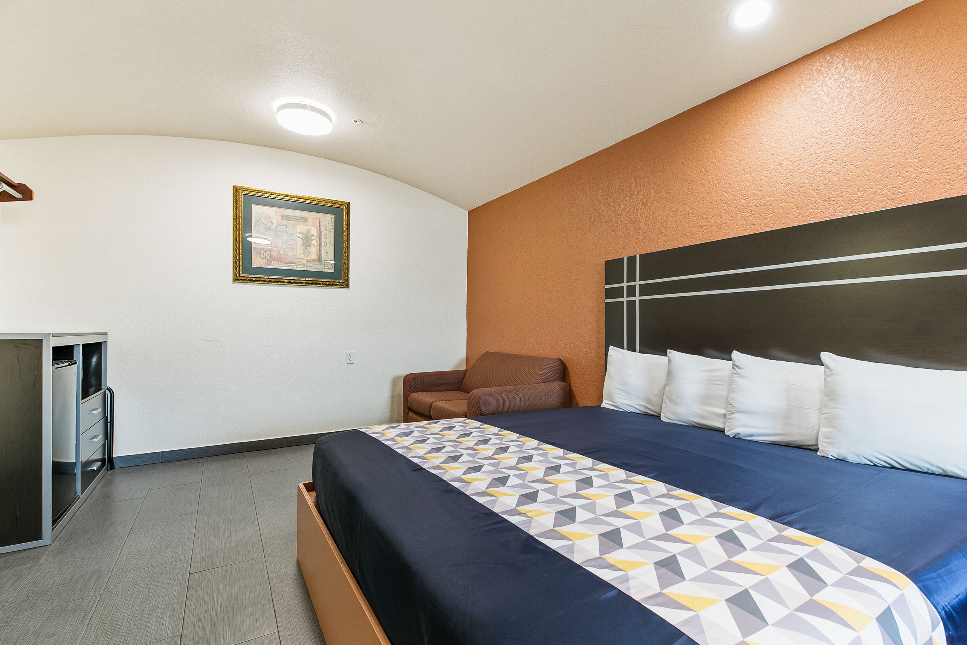 A hotel room with a bed, a desk, a chair, and a framed picture on the wall.