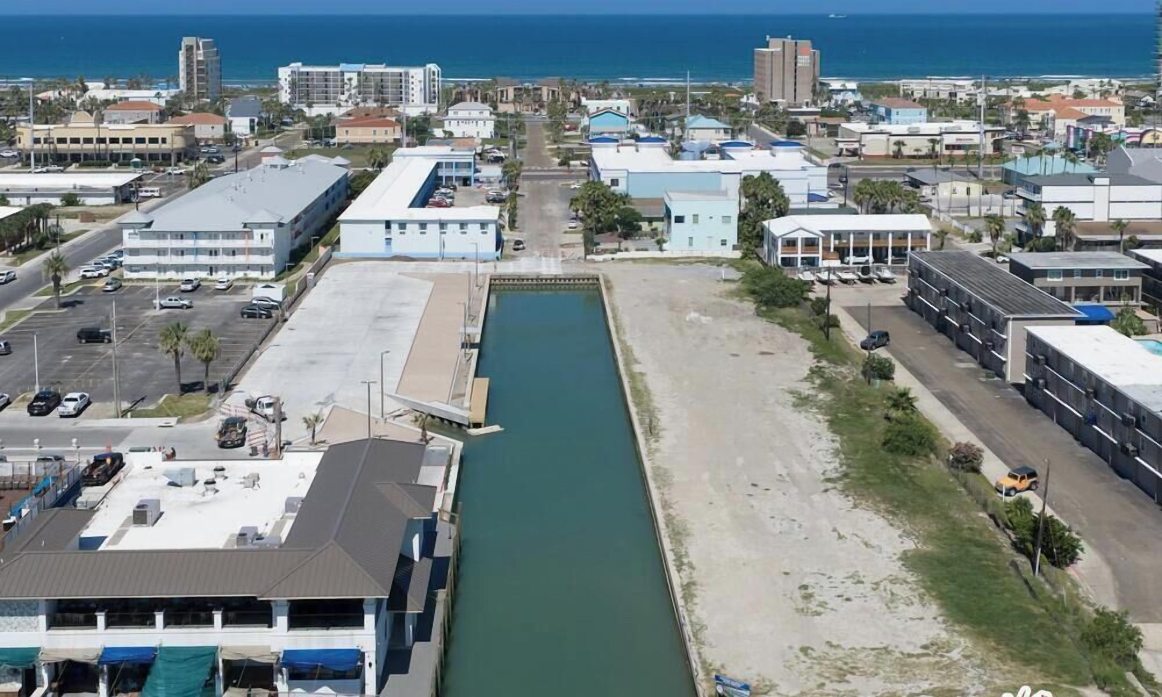 A coastal urban area with a narrow waterway, buildings, and a parking lot.