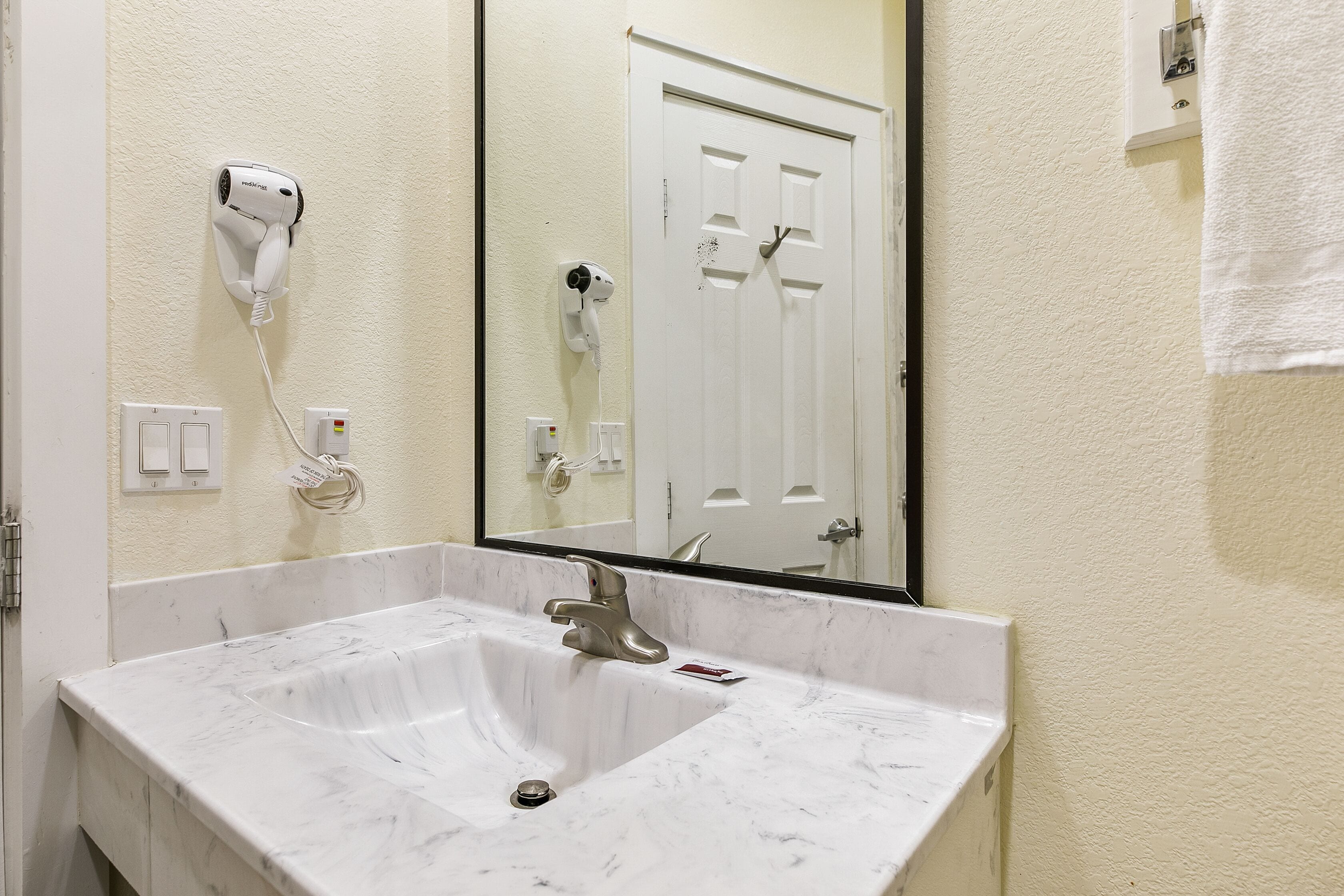 Une salle de bain avec un lavabo en marbre, un sèche-cheveux et un miroir qui reflète une porte.