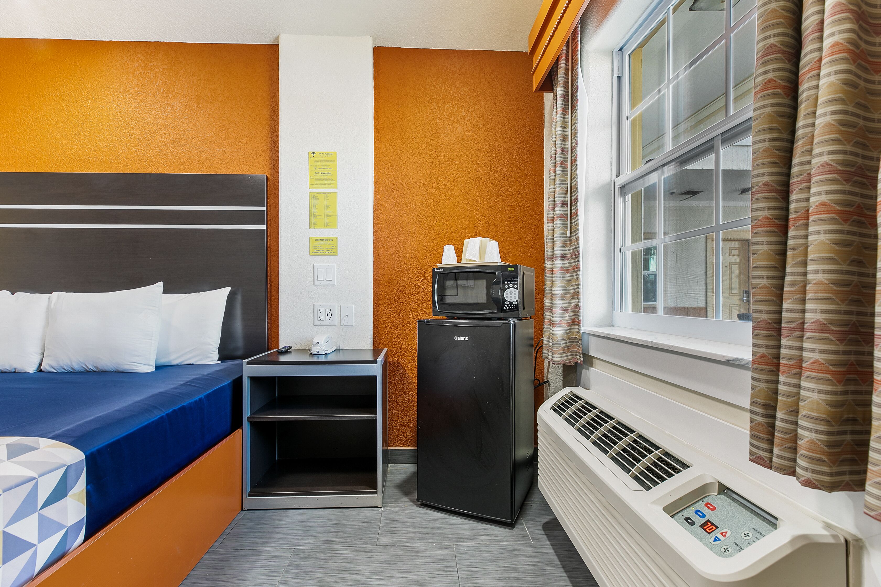 Habitación de hotel con cama, un refrigerador negro pequeño, microondas, calentador y ventana con cortinas.