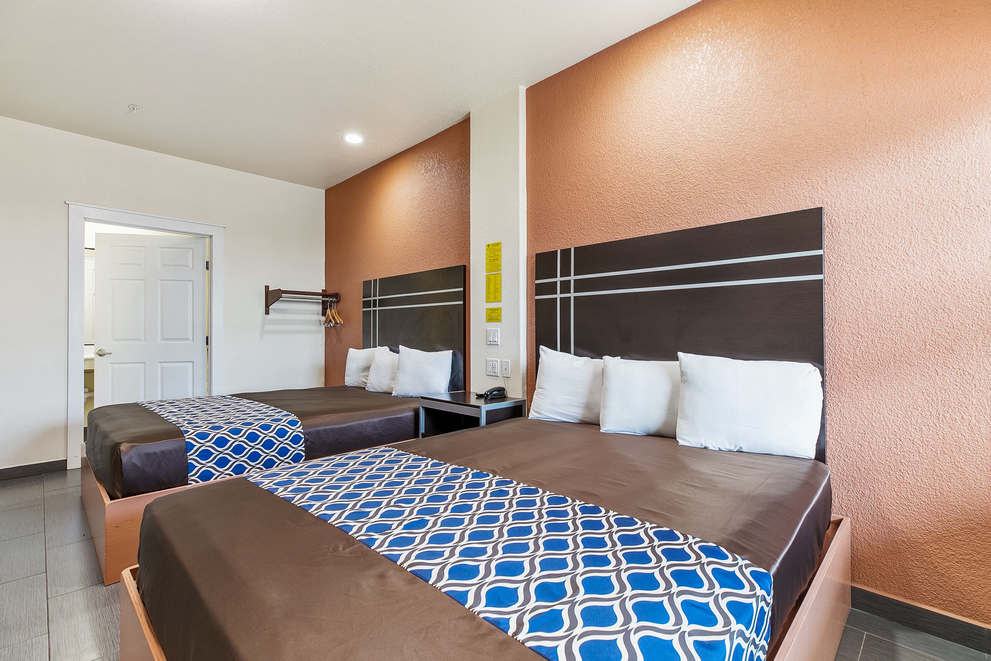 Una habitación de hotel con dos camas, cabecero de madera, mesita de noche y una puerta.