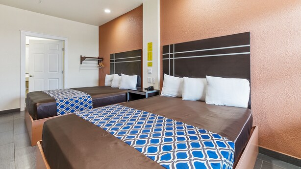 Habitació d'hotel amb dos llits, un capçal de fusta, una taula de nit i una porta.