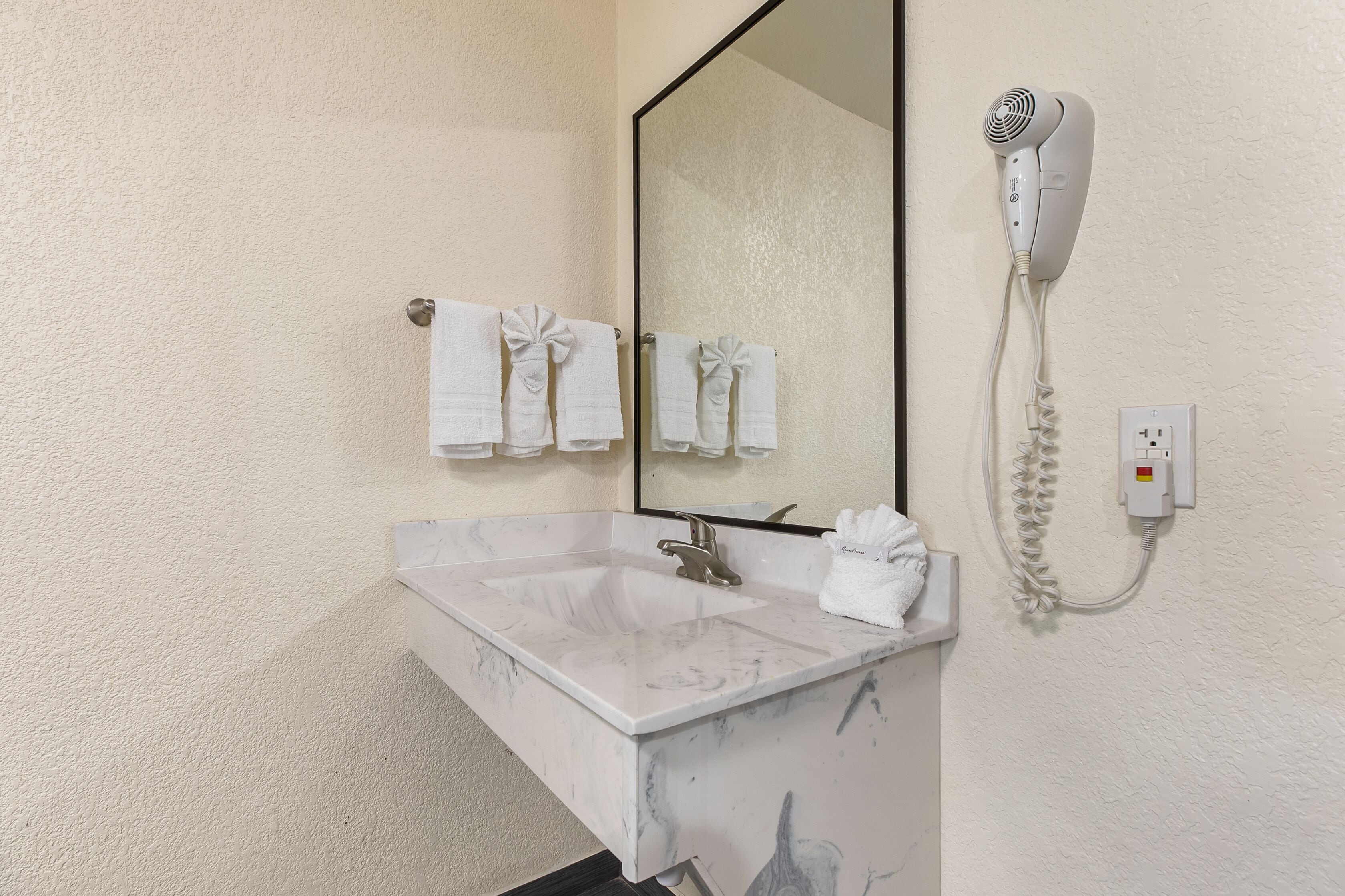Une salle de bain avec un lavabo en marbre, un grand miroir et un sèche-cheveux fixé au mur.