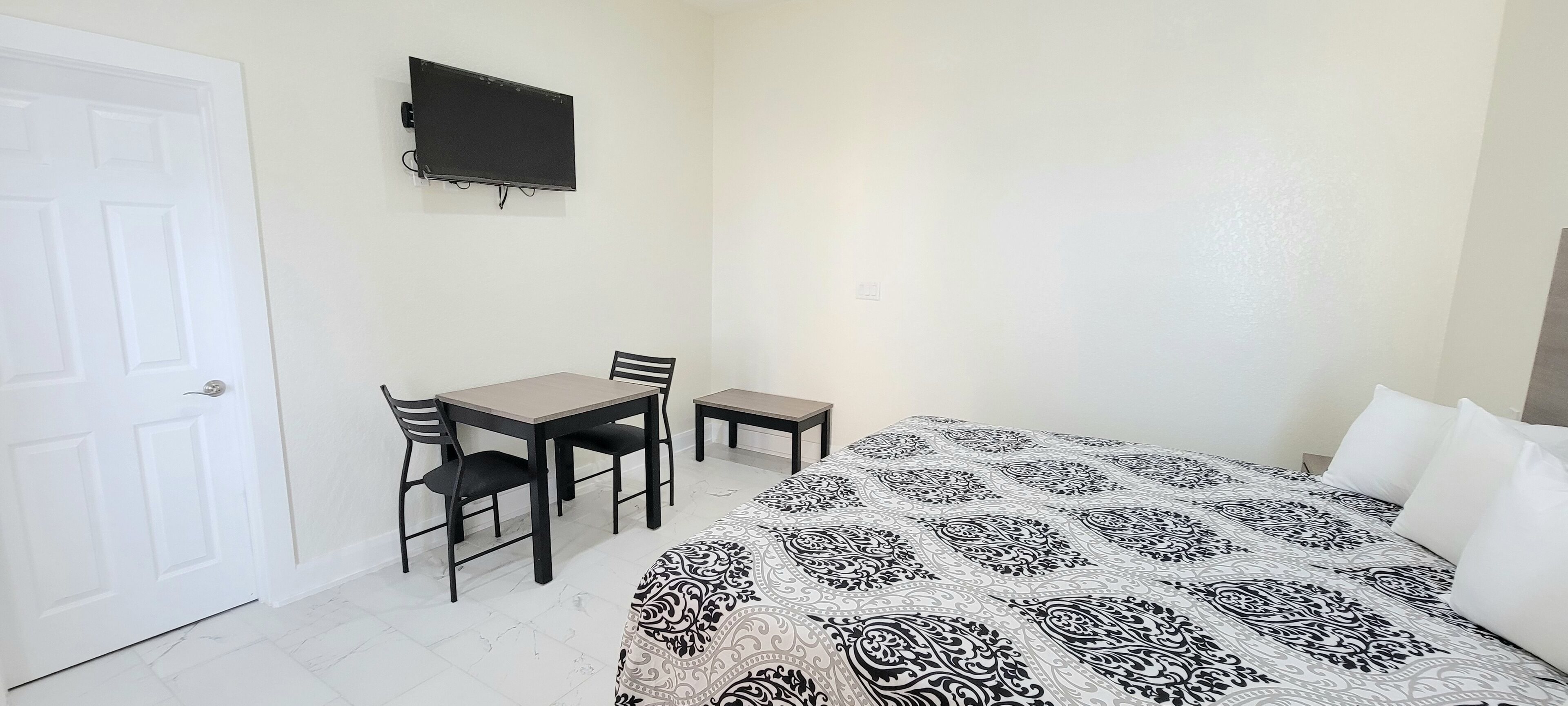 Een slaapkamer met een bed, een bureau, twee stoelen, een televisie en een witte deur.