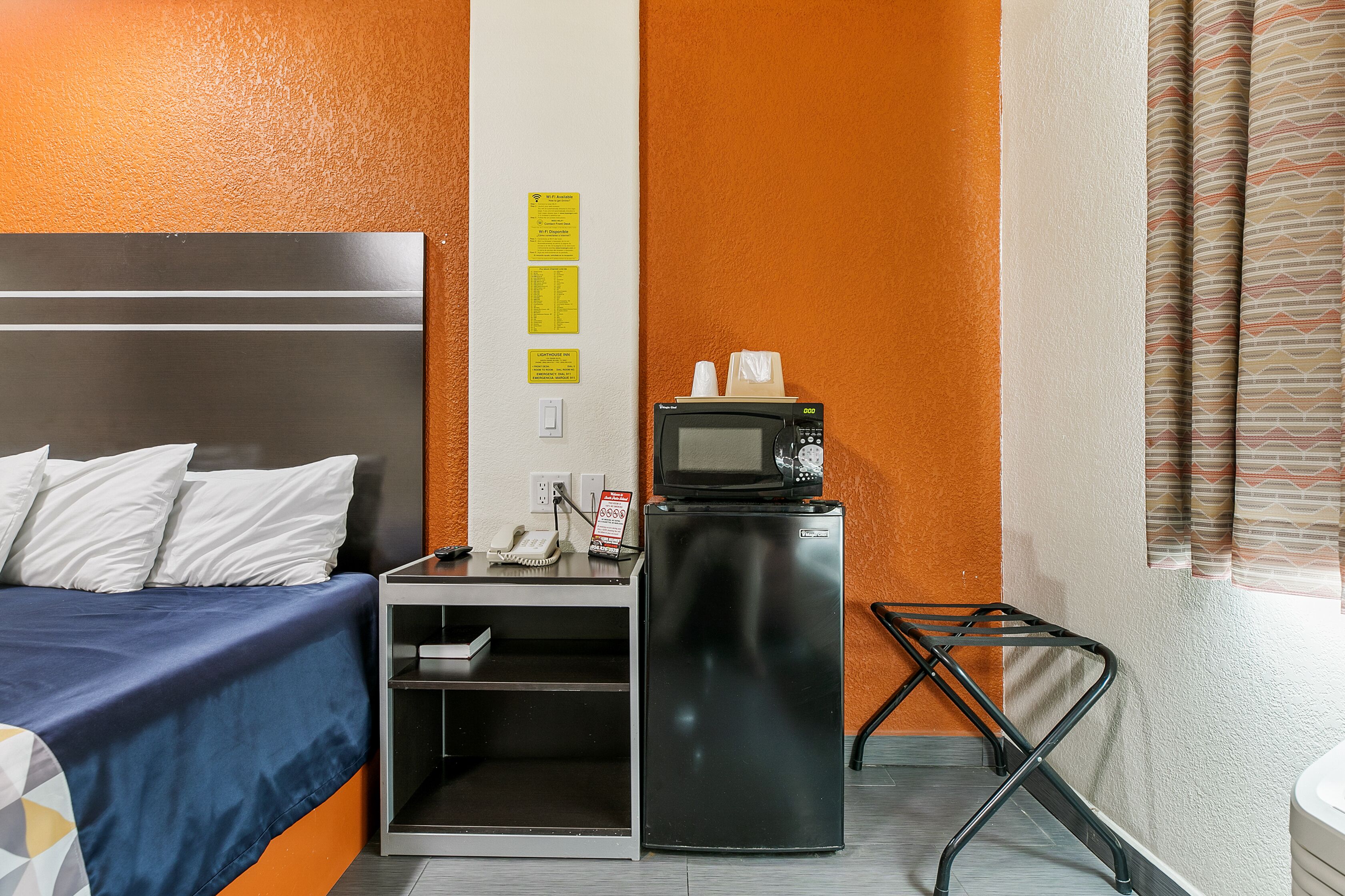 Et hotelværelse med seng, skrivebord med mikroovn, telefon og lille køleskab.