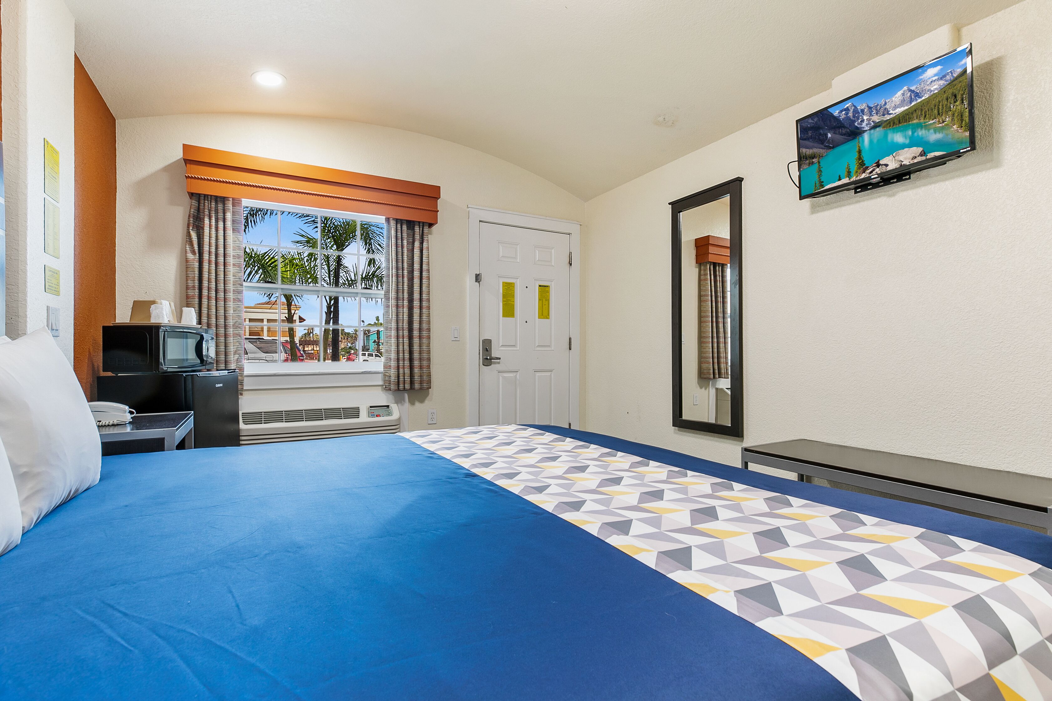 A hotel room with a bed, a television, a desk with a phone, and a window with curtains.