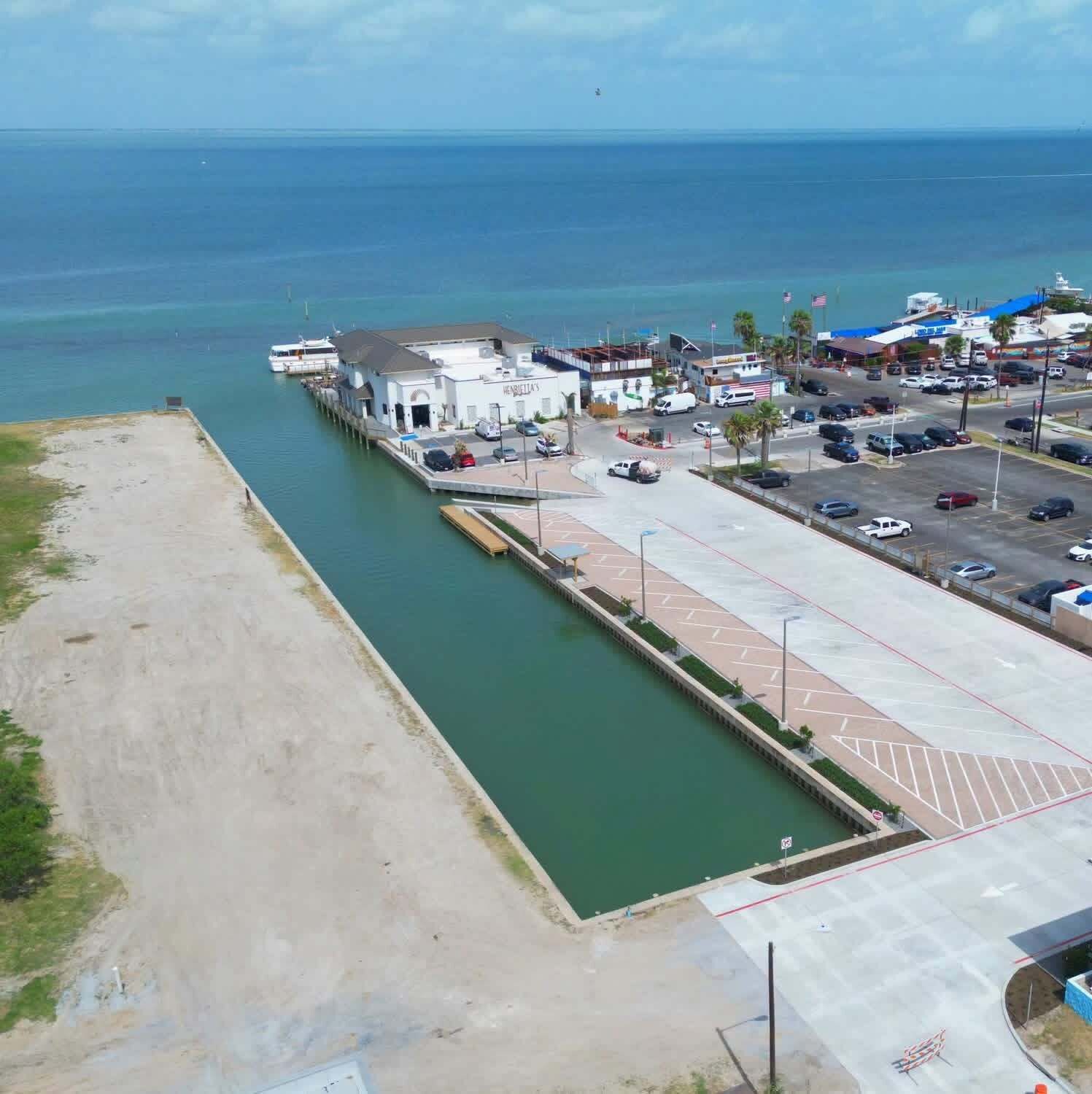 Uma marina costeira com um edifício branco, um estacionamento e vista clara do oceano.