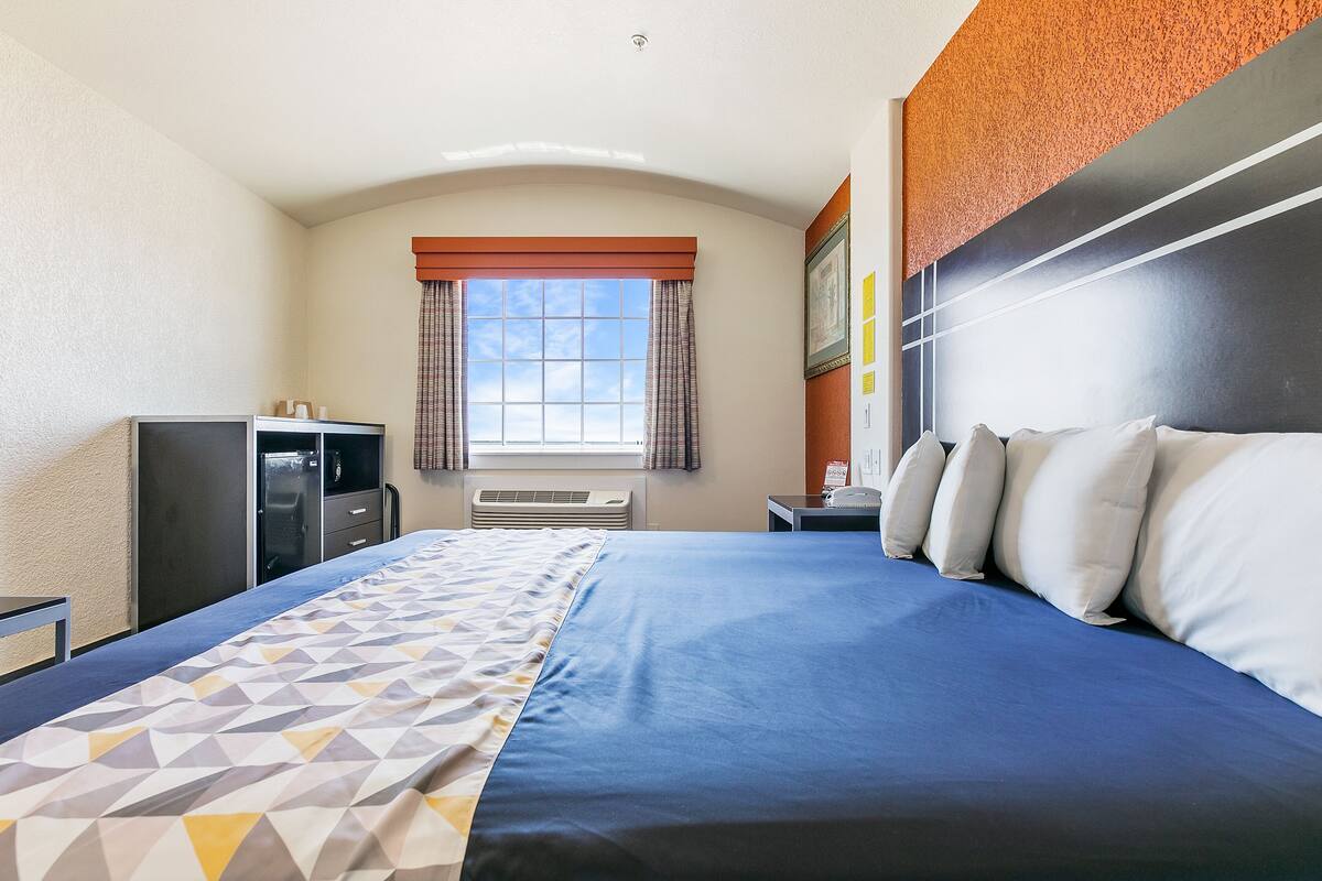 A hotel room with a large bed, a desk, a wardrobe, and a window with curtains.