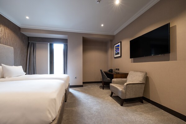 A hotel room with two beds, a desk, a chair, a flat-screen TV mounted on the wall, and a large window with curtains. - DoubleTree by Hilton Belfast City Ten Square (Belfast)