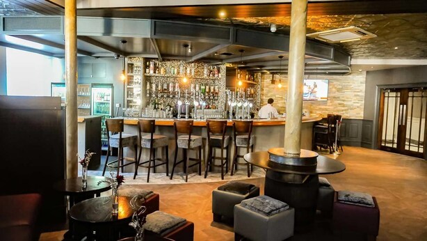 Una zona de bar con taburetes, una barra y una pantalla de televisión.