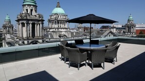 Terraza en la azotea con una mesa redonda y sillas, una sombrilla negra y vistas de edificios históricos con cúpulas.
