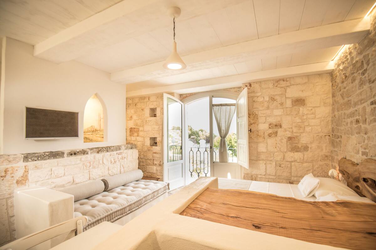 A bedroom with a wooden bed, a cushioned bench, and a stone wall.