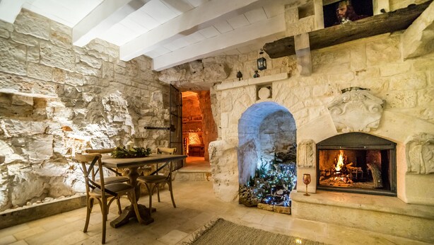 A stone-walled room with a fireplace, a table with chairs, and a Christmas tree. - La Corte dell'Astore (Alberobello)