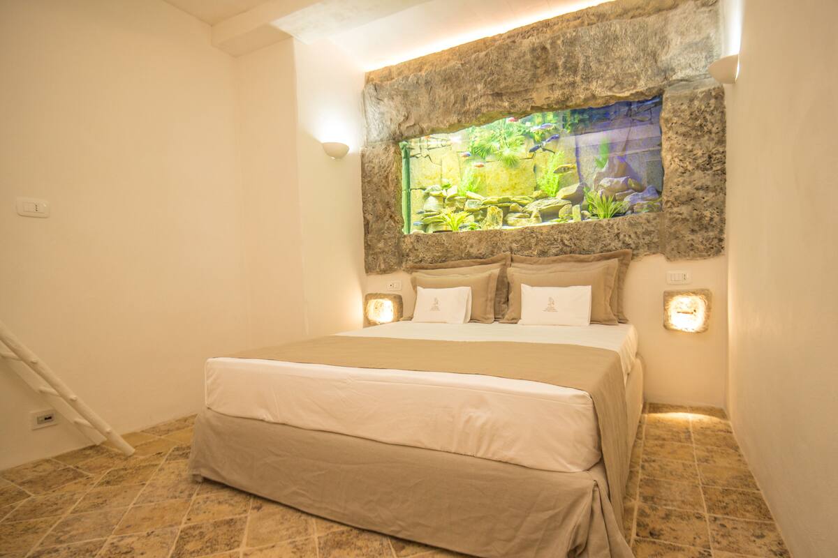 A bedroom with a bed, a stone wall, and a fish tank.