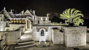 A stone building with a central staircase, a bell, and a palm tree. - La Corte dell'Astore (Alberobello)
