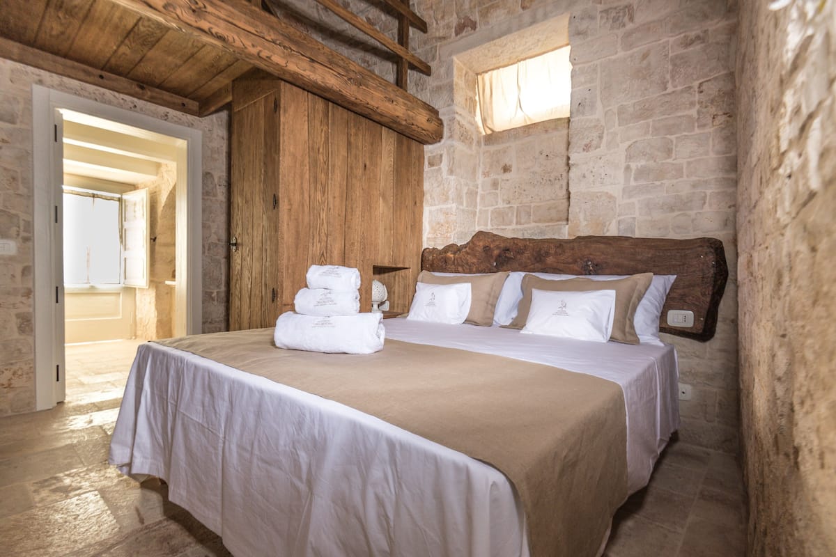 A bedroom with a large bed, stone walls, and a wooden ceiling.