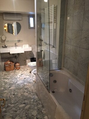 Un baño con ducha de vidrio, bañera, lavamanos con espejo e inodoro.