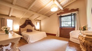 Un dormitorio con una cama grande, una mesita de noche, una silla, una ventana con cortinas y un techo de madera.