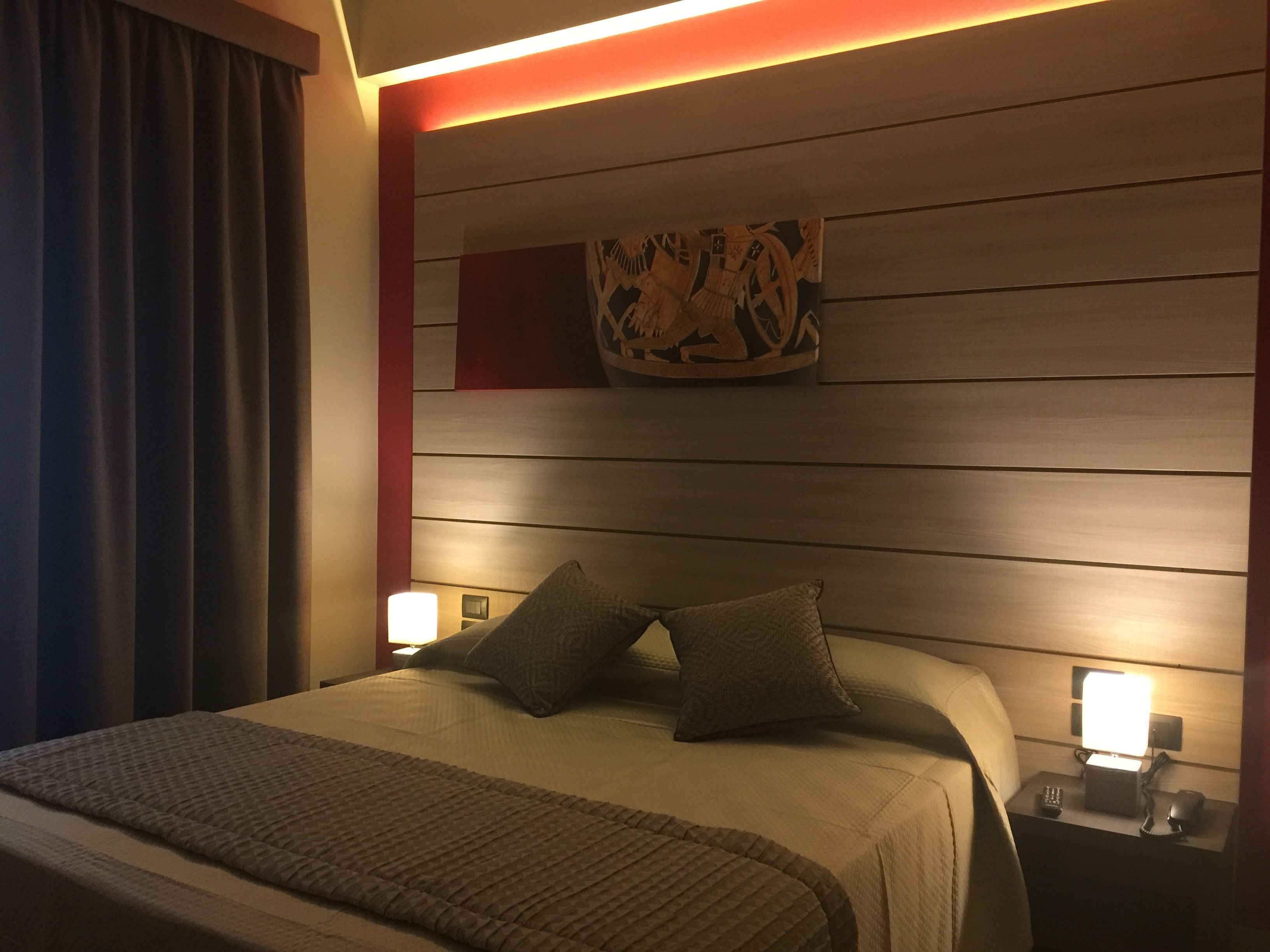 Habitación de hotel con una cama, dos mesitas de noche, una lámpara de noche, una obra de arte en la pared y una cortina.