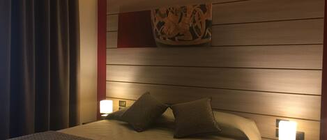 Habitación de hotel con una cama, dos mesitas de noche, una lámpara de noche, una obra de arte en la pared y una cortina.