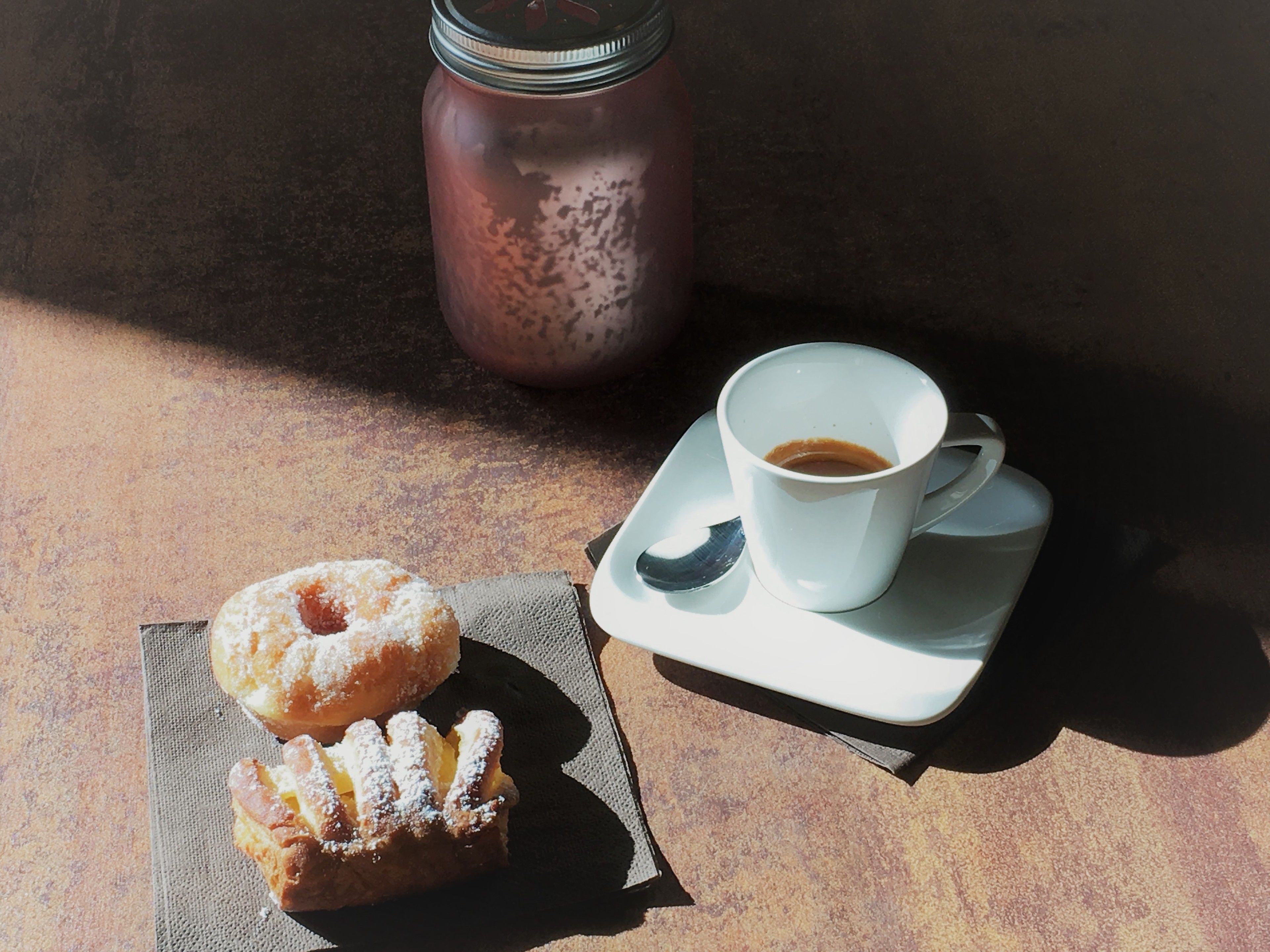 Una mesa con una taza de café, un tarro y dos pasteles.