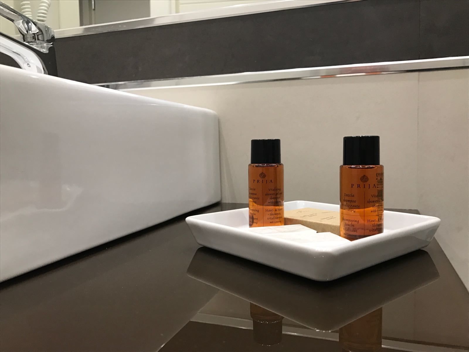 A bathroom with a white sink and two bottles of shampoo on a white tray.