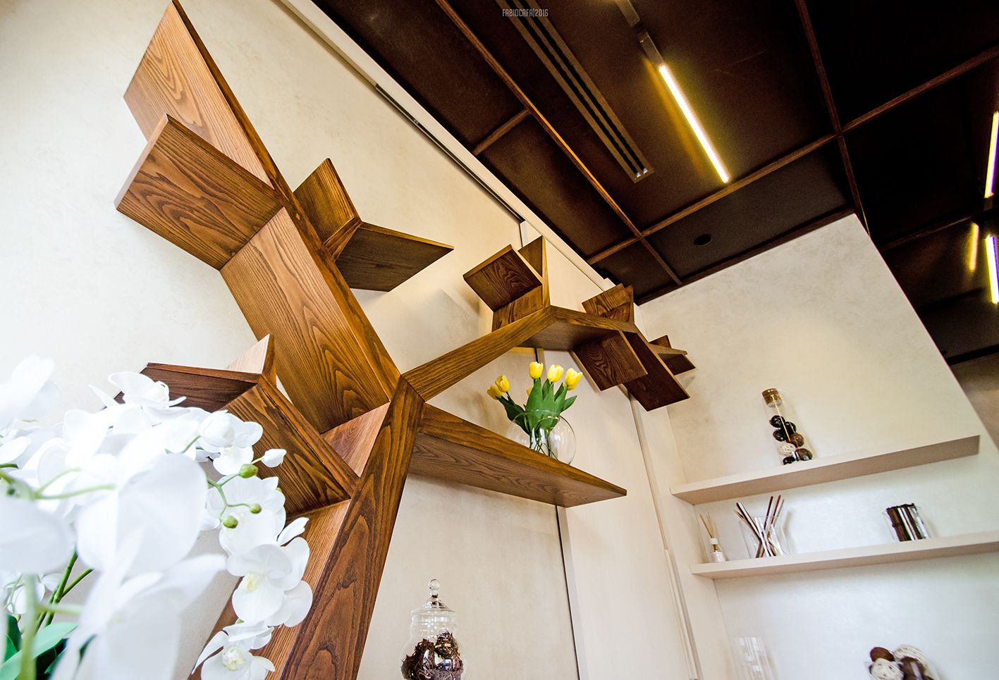 A wooden cross structure with a vase of yellow flowers and a glass jar with dried flowers.