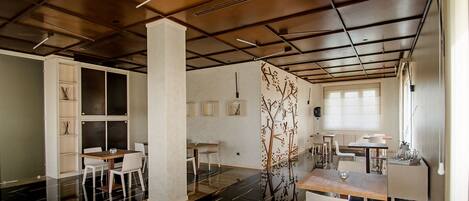 A modern interior with a black and white color scheme, featuring a dining area with white chairs and a wooden table, a white bookshelf, and a decorative wall piece.