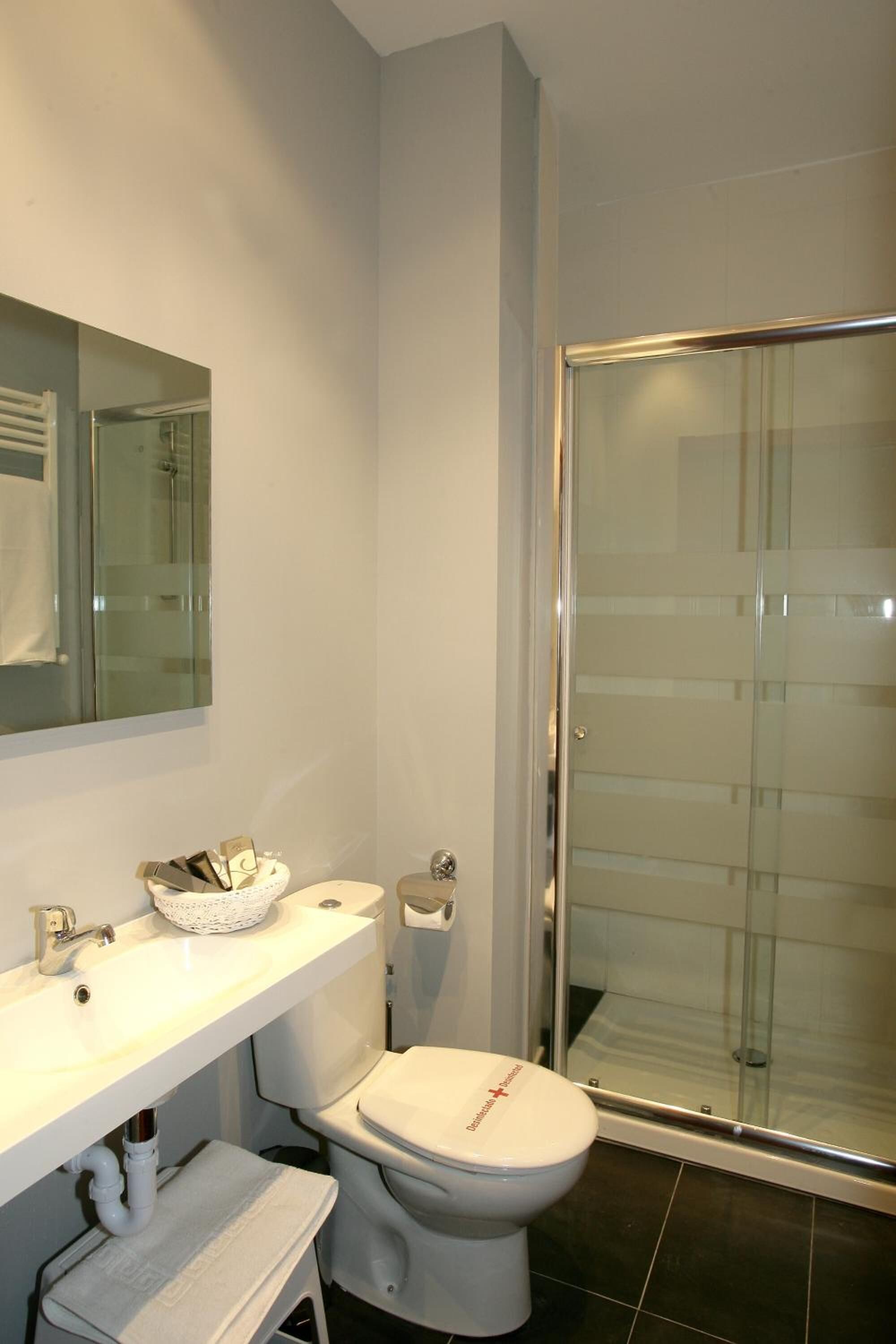 Un baño moderno con cabina de ducha de vidrio, inodoro blanco y lavabo con espejo superior.