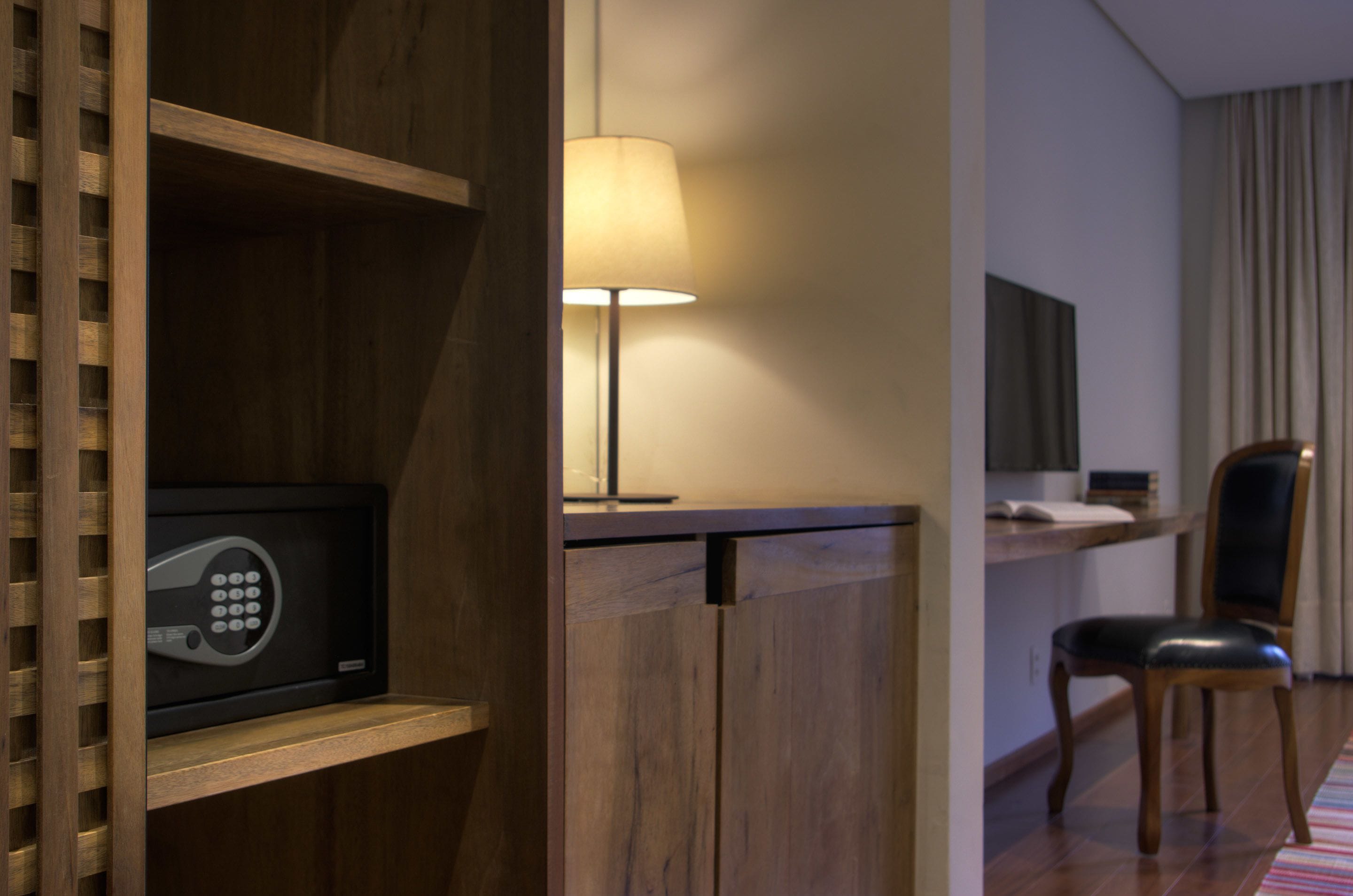 Una habitación de hotel con un escritorio de madera, una lámpara, una silla y una caja fuerte.
