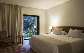 A hotel room with a large bed, a chair, a small table, and a view of greenery through a window. - Hotel Villa Amazonia (Manaus)
