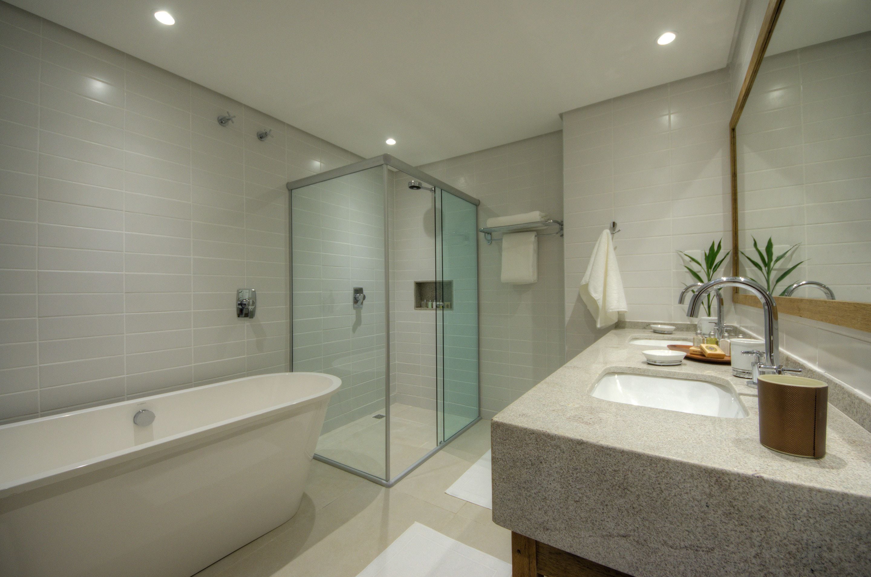 Un baño moderno con una bañera independiente, cabina de ducha con mampara de cristal y encimera de granito con lavamanos y espejo.