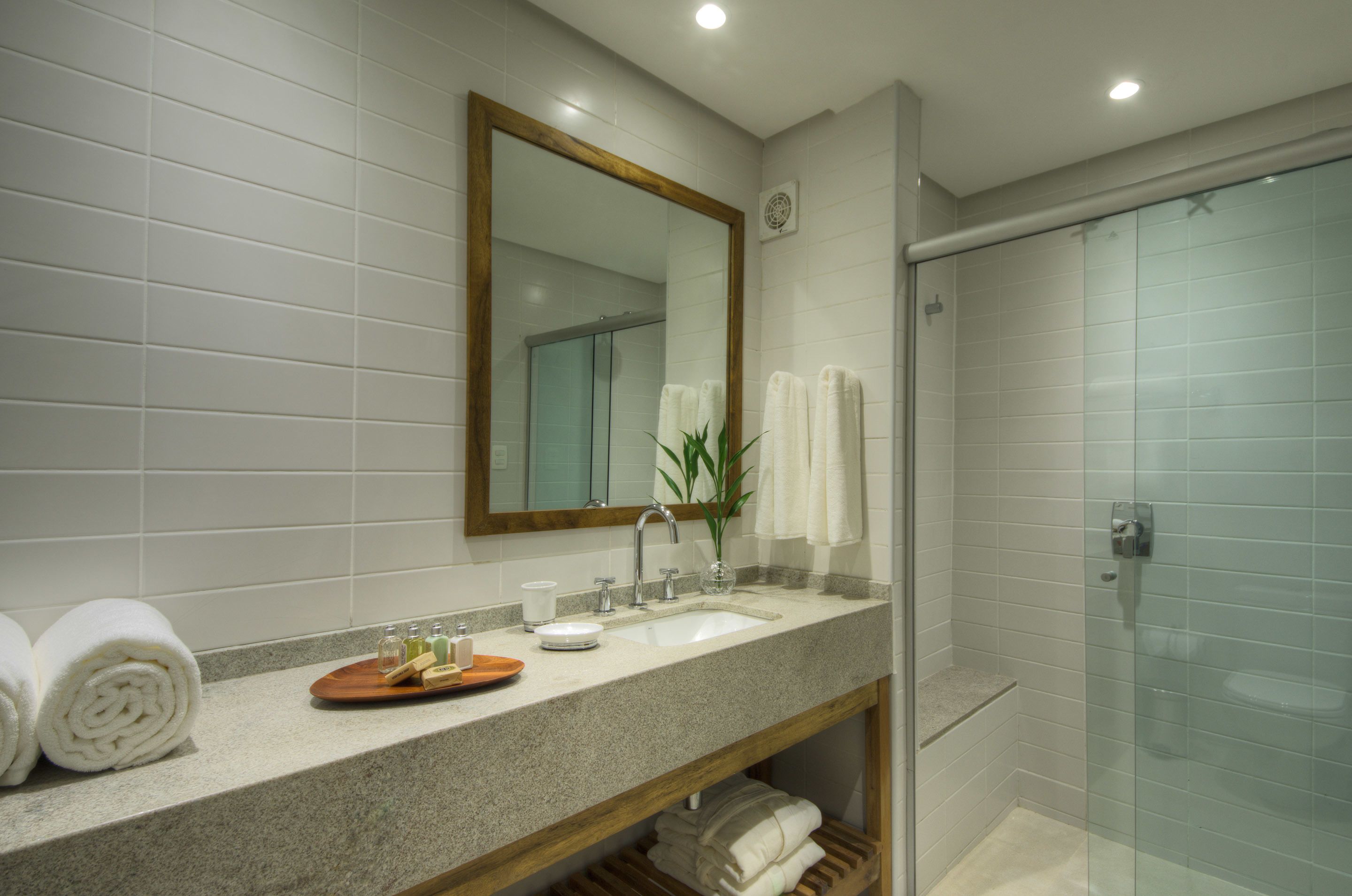 A bathroom with a granite countertop, a wooden vanity, a large mirror, a glass shower enclosure, and neatly folded towels.