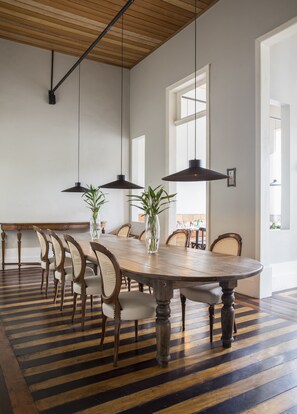 A dining area with a large wooden table, several chairs, hanging pendant lights, and a striped floor. - Hotel Villa Amazonia (Manaus)