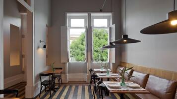 A dining area with tables set for two, a bench, and a view of greenery outside.