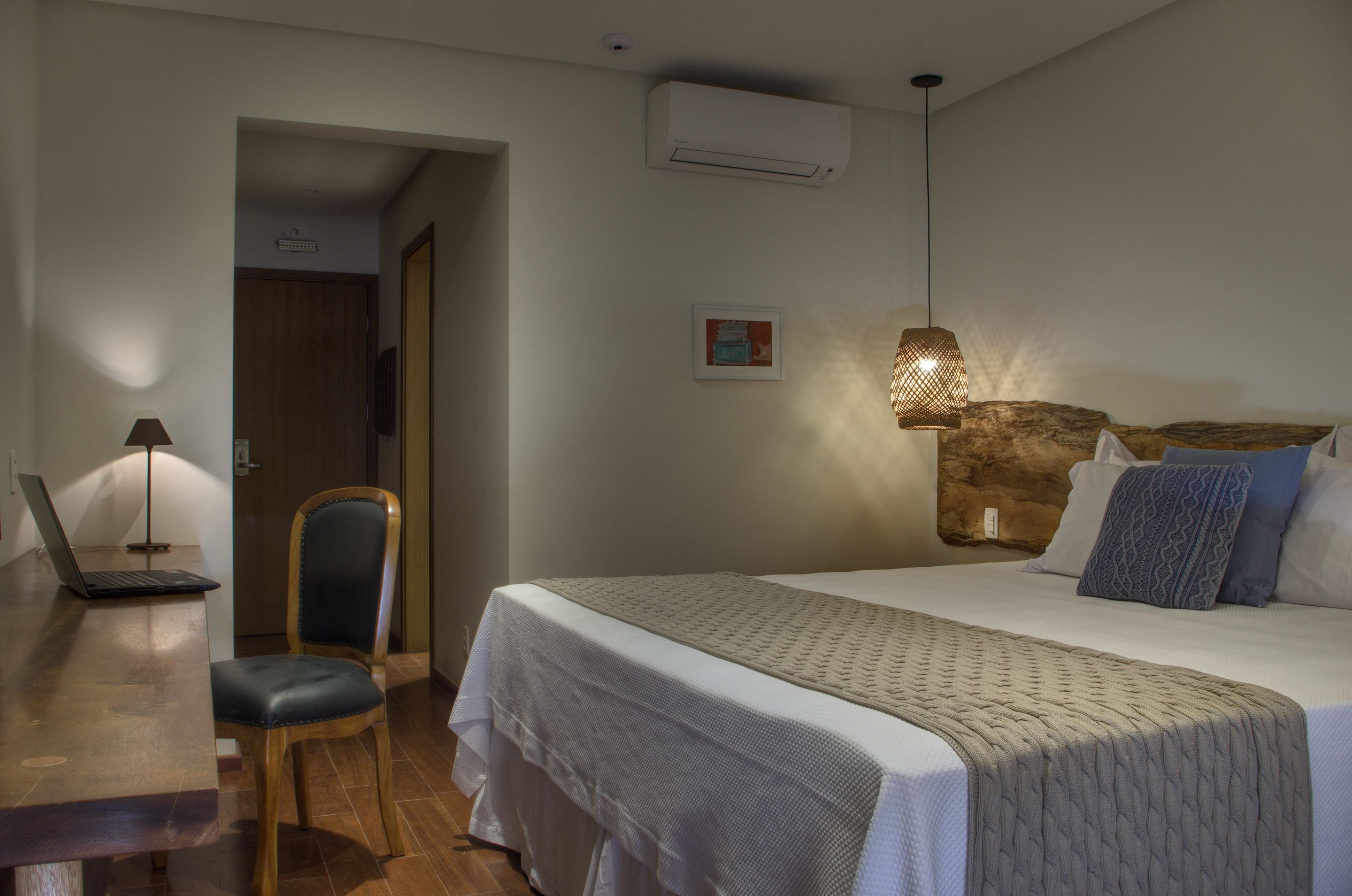 Una habitación de hotel con cama, escritorio, laptop, silla y aire acondicionado de pared.