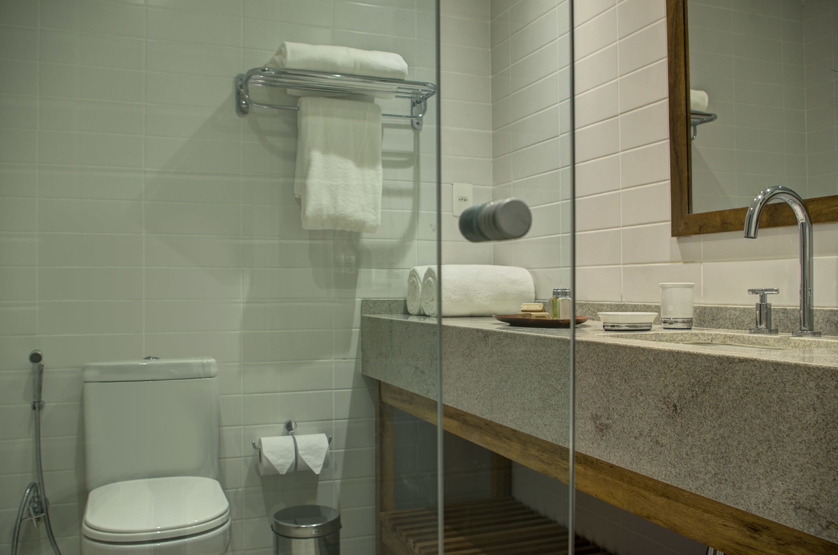A bathroom with a toilet, sink, and mirror. There are towels and toiletries on the sink counter.