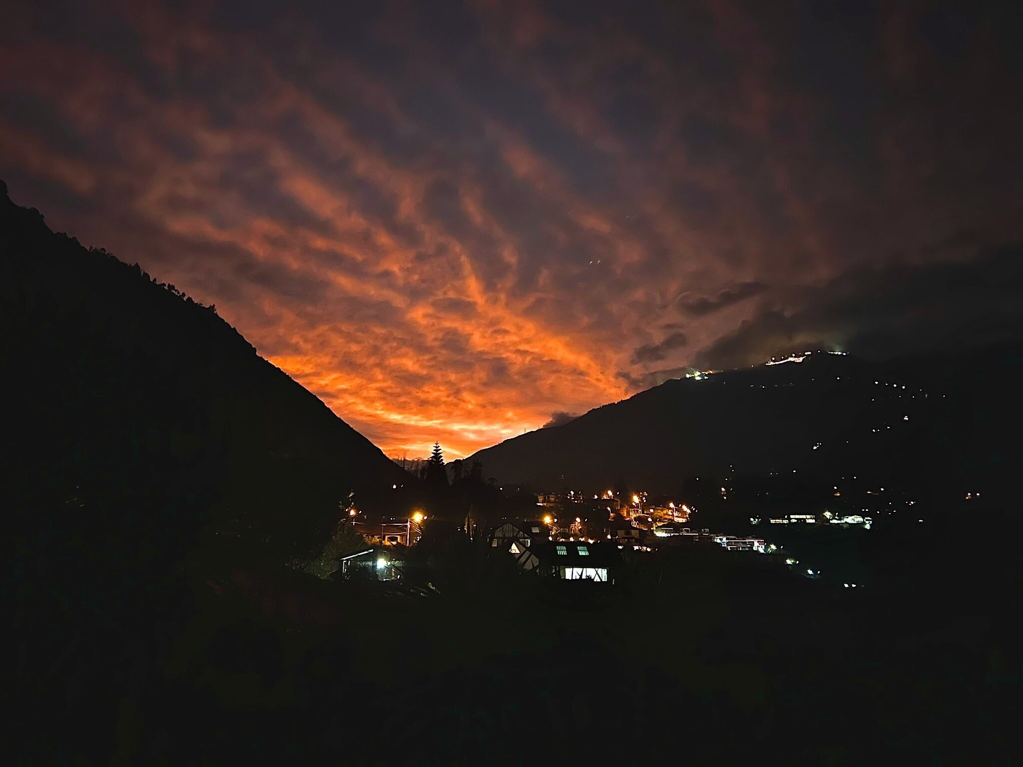 Une vue nocturne d’une vallée, avec une ville au premier plan et des montagnes en arrière-plan.