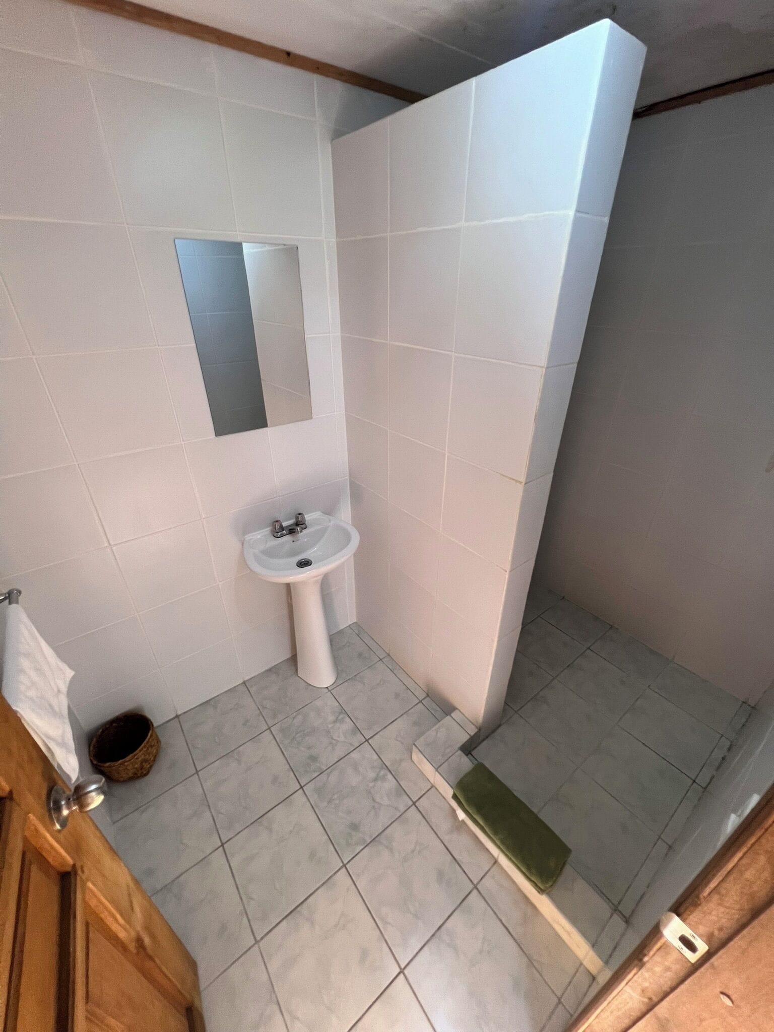 Un baño pequeño con lavamanos blanco, espejo y zona de ducha.