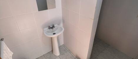 Un baño pequeño con lavamanos blanco, espejo y zona de ducha.