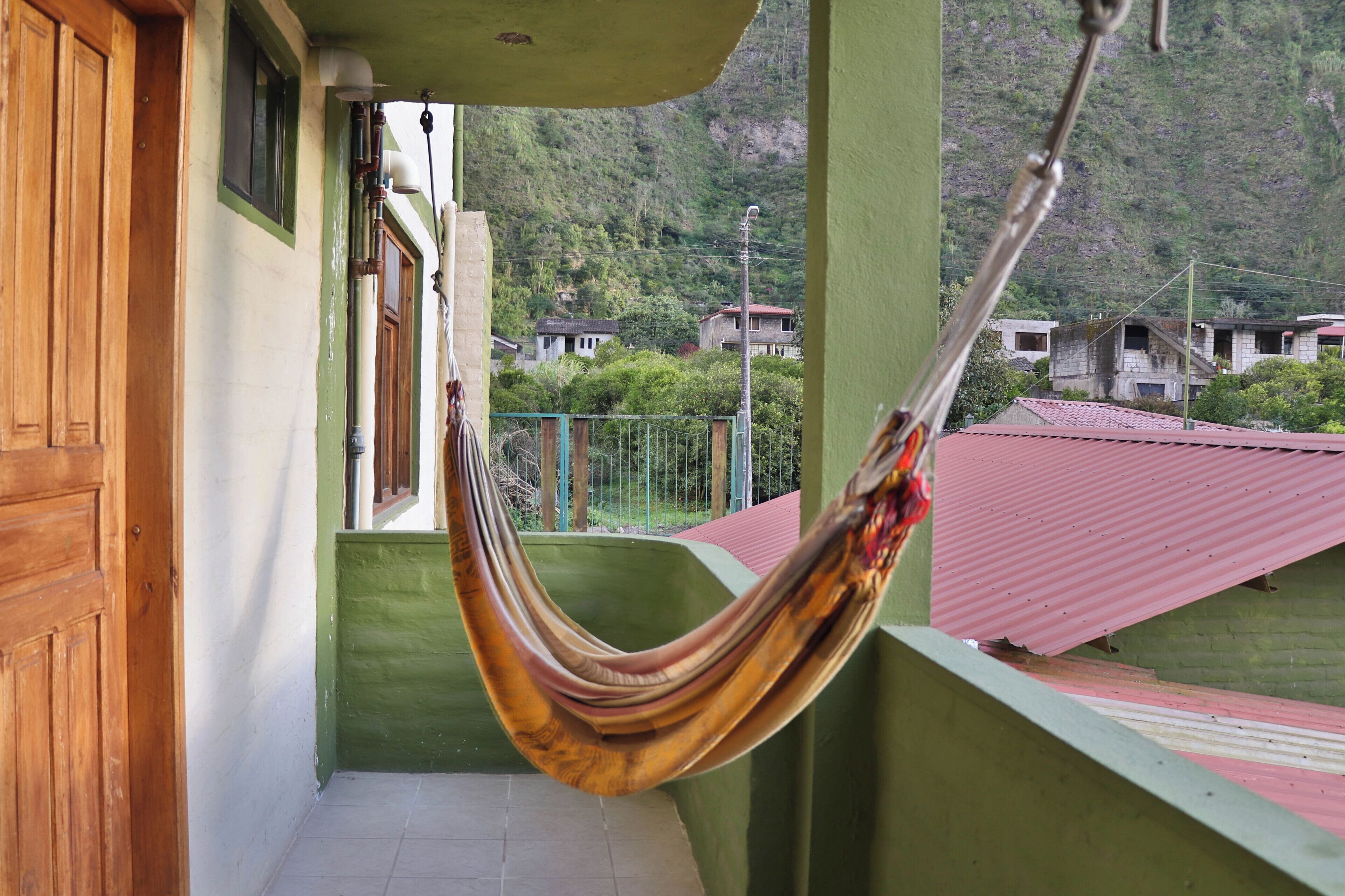 A hammock hanging on a balcony with a view of houses and greenery in the background.