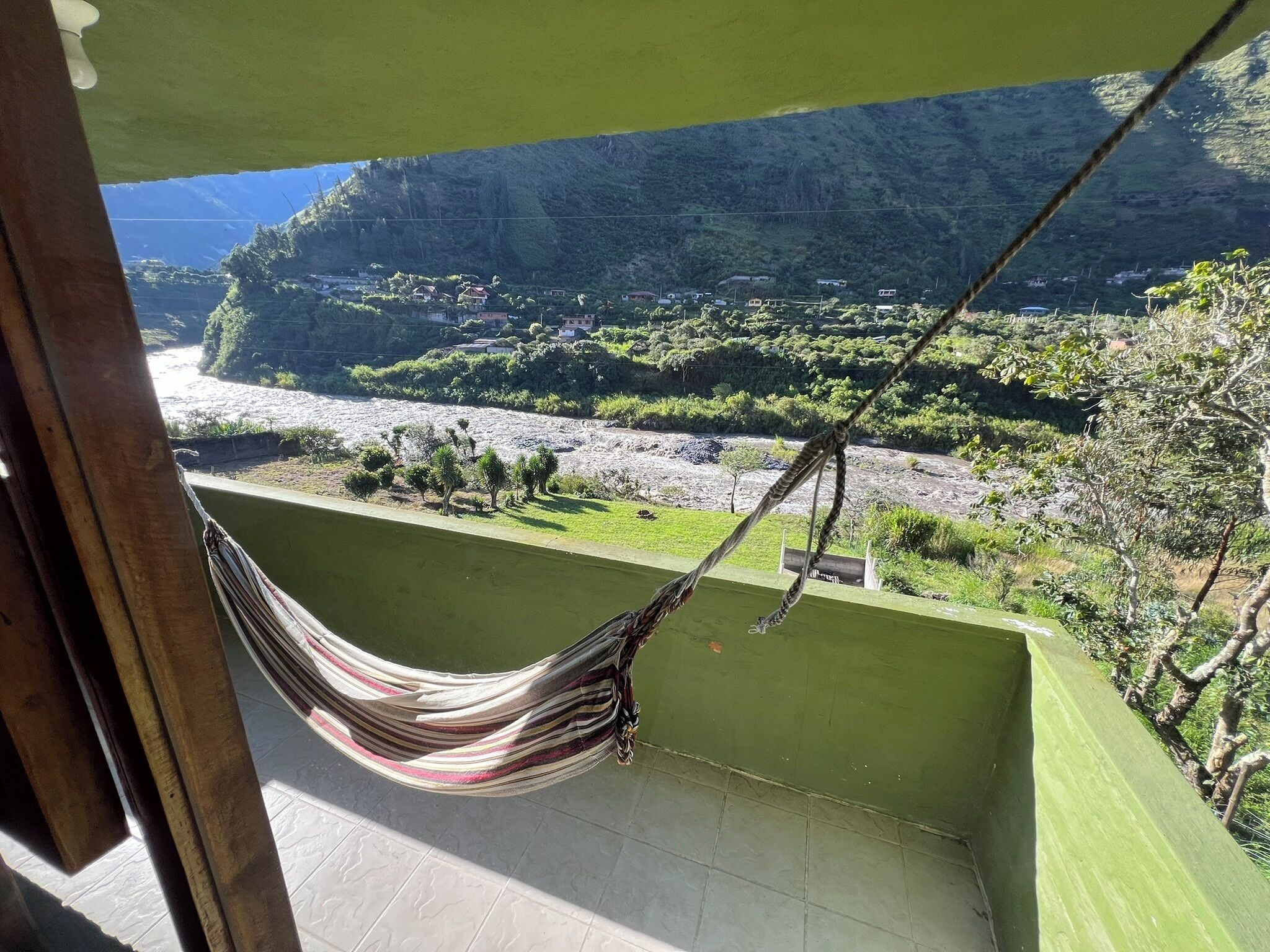 Un balcón con una hamaca, vista a un río y un paisaje montañoso.