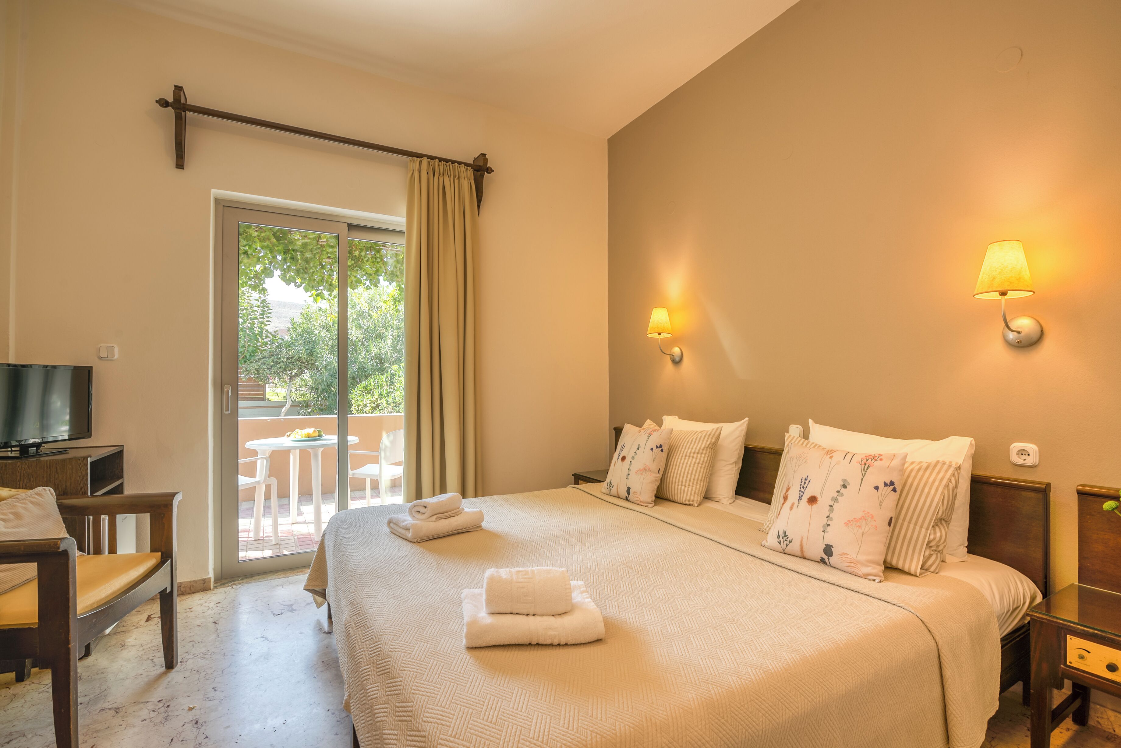 A hotel room with a large bed, two bedside lamps, a TV, and a view of the outdoors.