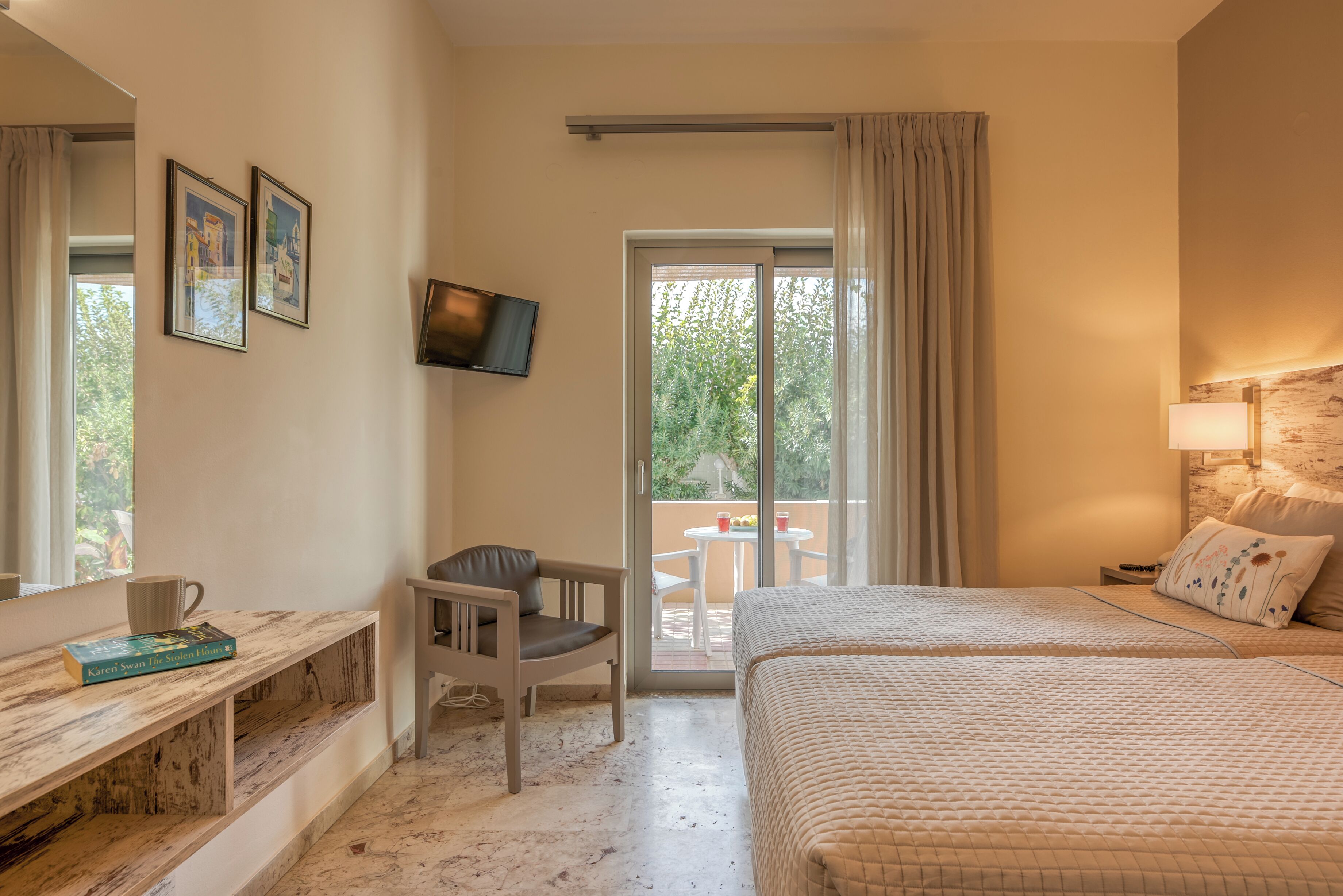 A hotel room with a bed, a desk, a chair, a TV, and a balcony with a table and chairs.
