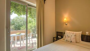 Habitación de hotel con cama, mesita de noche, lámpara, ventana con cortinas y vista a un patio exterior con sillas y mesa.
