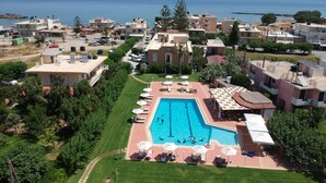 A hotel with a swimming pool surrounded by lounge chairs and umbrellas, set against a backdrop of a coastal landscape. - Peli Hotel (Kissamos)