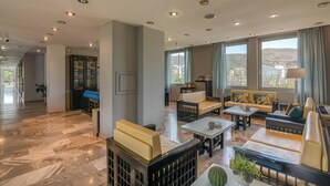 A spacious living area with multiple seating options, a fireplace, and large windows offering a view of the outdoors. - Peli Hotel (Kissamos)