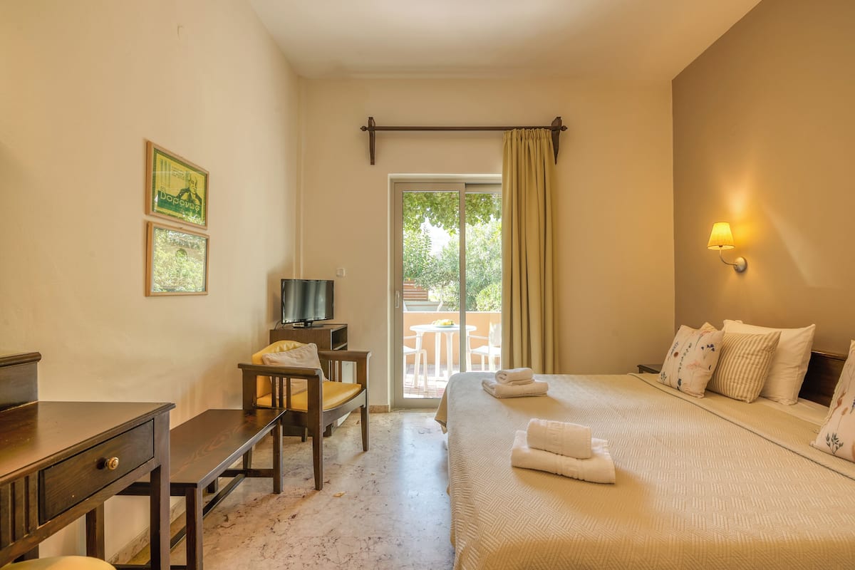 A hotel room with a bed, a desk, a chair, a television, and a balcony with a table and chairs.