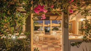 An outdoor patio area with tables and chairs, surrounded by greenery and pink flowers. - Peli Hotel (Kissamos)