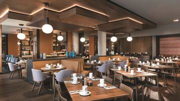 A modern restaurant with wooden tables and chairs, pendant lighting, and a bar area.